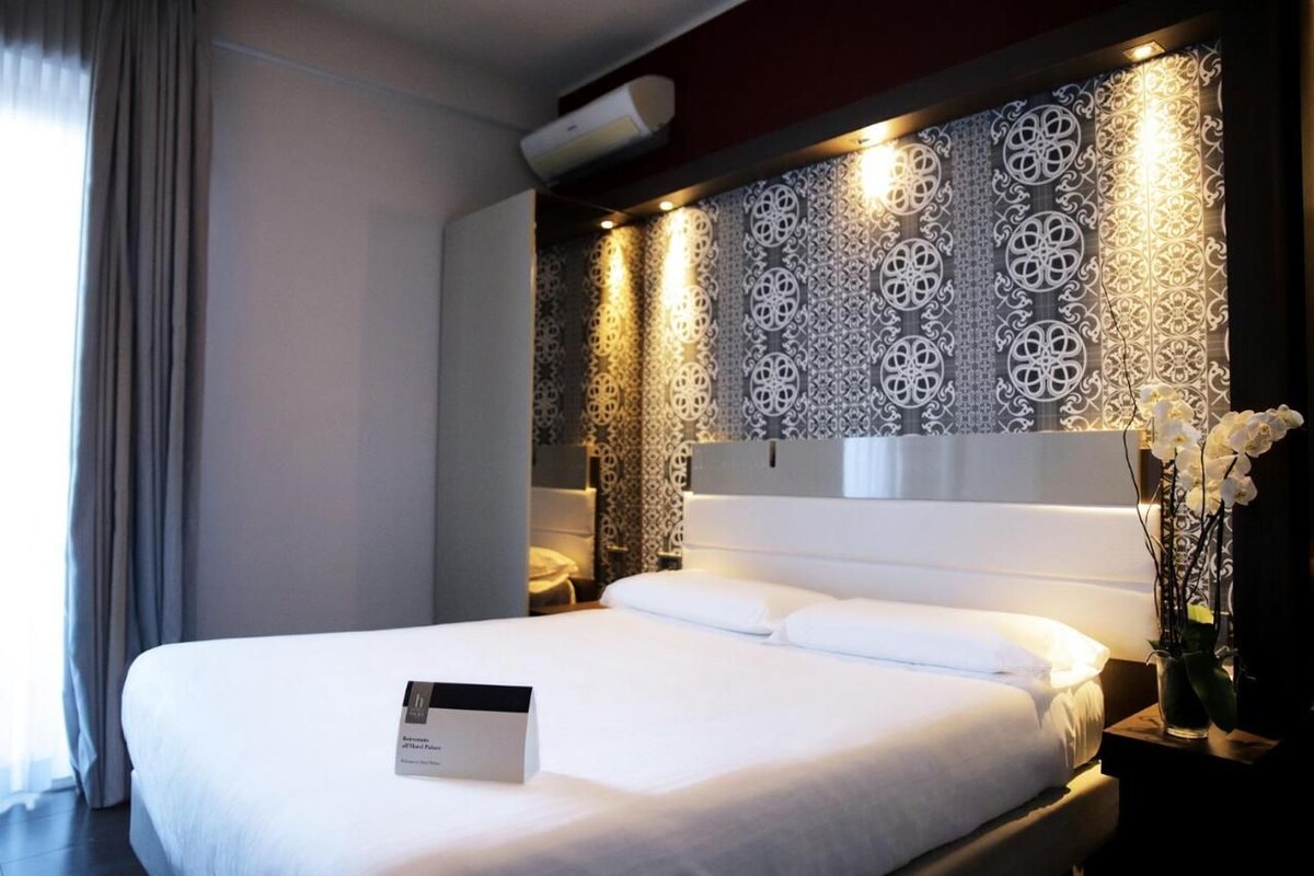 Una habitación de hotel con una cama grande, un cabecero decorativo y una mesita de noche con un jarrón de flores.