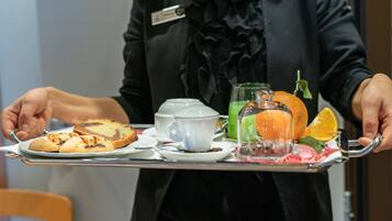 A person holding a tray with a teapot, a glass of green drink, an orange, and a slice of cake.