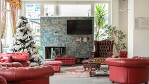 A living room with red leather sofas, a large flat-screen TV mounted on a stone wall, and a Christmas tree. - Hotel Palace (Battipaglia)