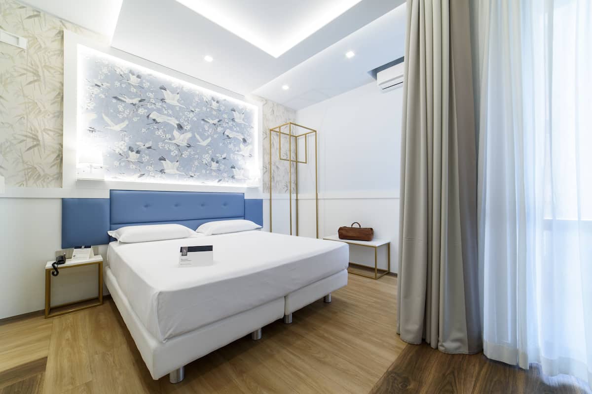 Ein modernes Hotelzimmer mit einem großen Bett, einem Nachttisch, einem Wandbild und einem Fenster mit Vorhängen.