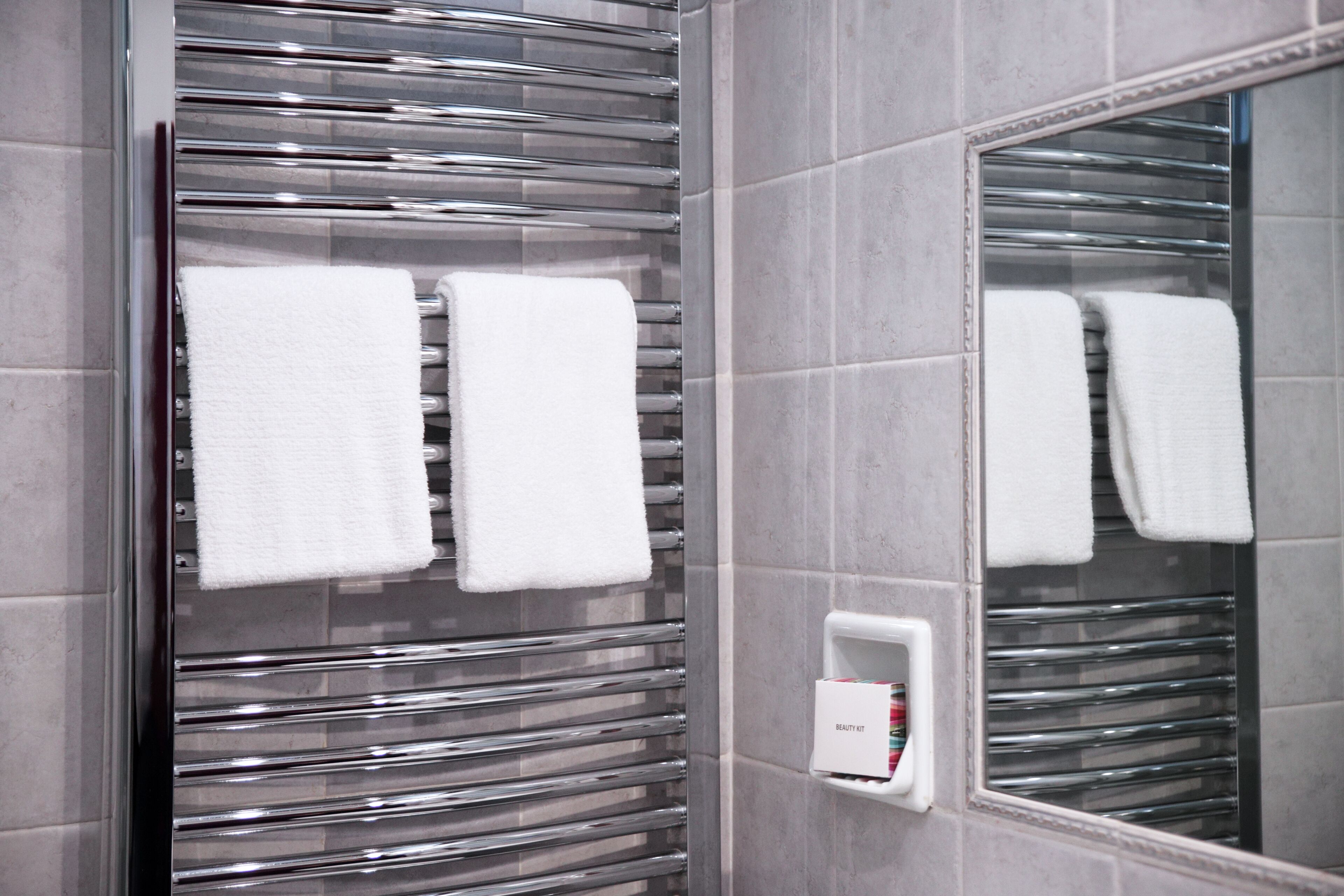 A bathroom with a glass shower enclosure, a white towel rack with three towels, and a vanity mirror.