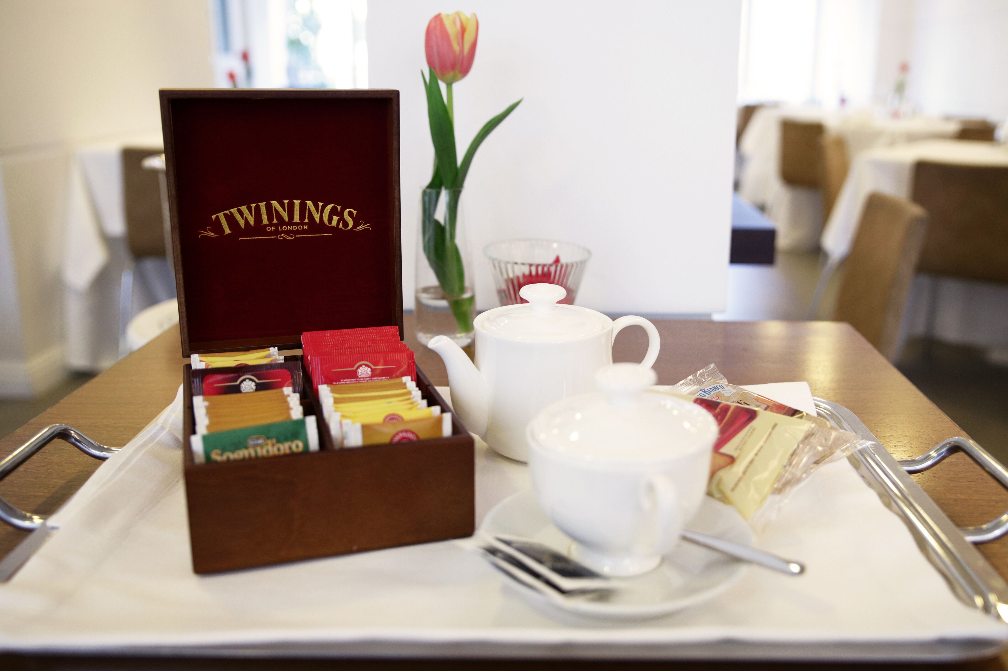 Una bandeja con cajas de té Twinings, una tetera, tazas y una tulipa.