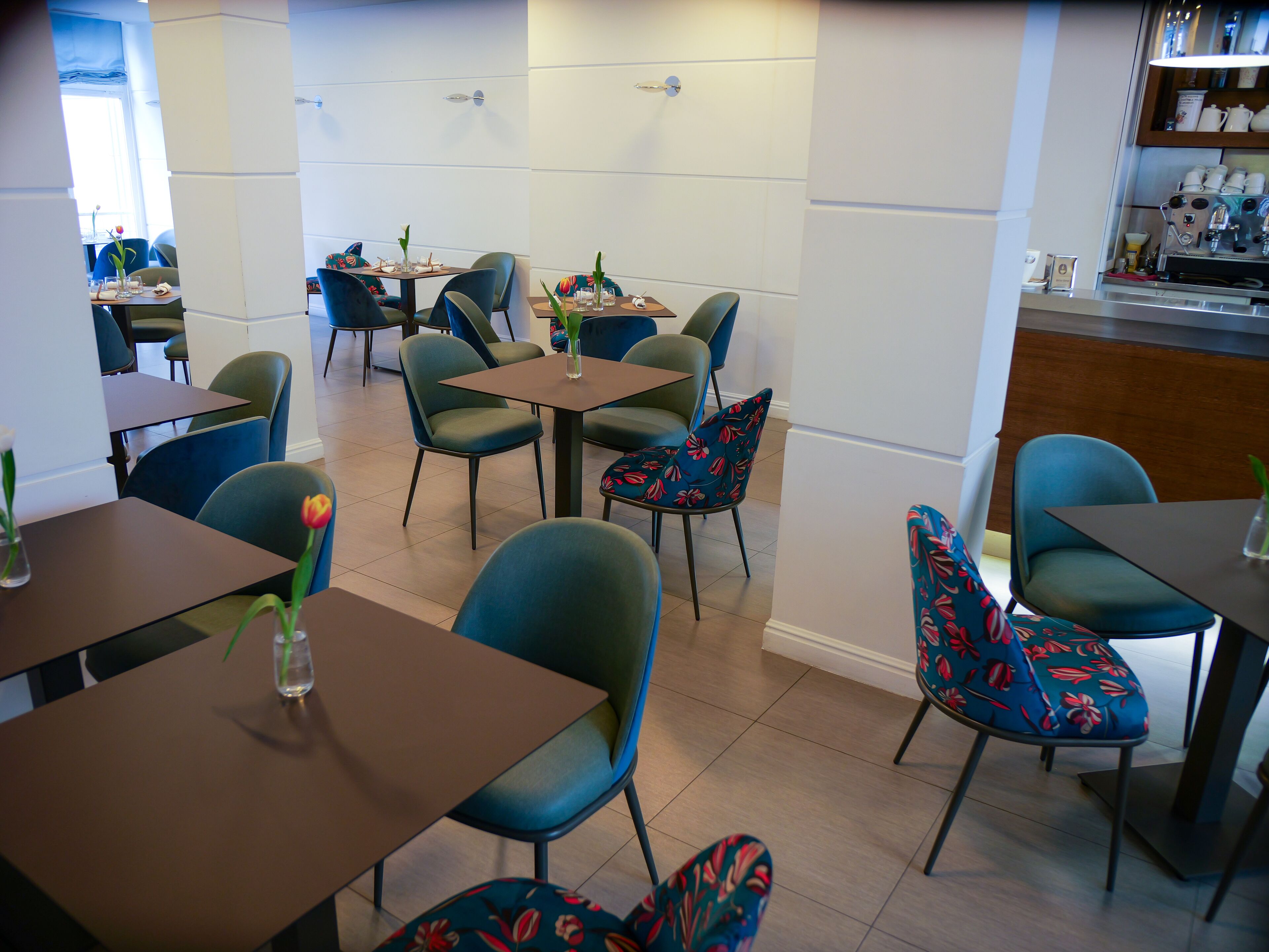 A modern dining area with multiple tables and chairs, a coffee machine, and a view of the street outside.