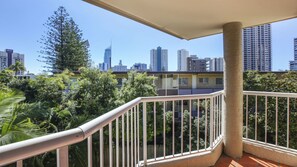 A balcony with a view of a city skyline, including high-rise buildings and a large tree. - Mari Court Resort (Surfers Paradise)
