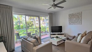 A modern living room with a large TV, two sofas, a coffee table, and a ceiling fan. - Mari Court Resort (Surfers Paradise)