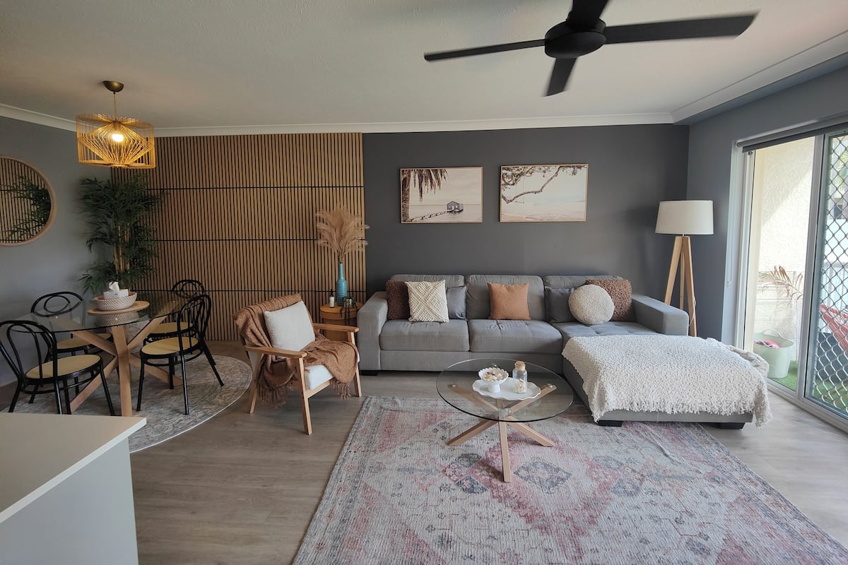 A modern living room with a grey sofa, a round coffee table, and a dining area with a glass table and chairs.