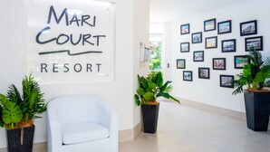 A reception area with a white chair, a sign reading "Mari Court Resort", and a wall decorated with framed pictures. - Mari Court Resort (Surfers Paradise)