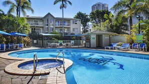 A swimming pool with a hot tub, surrounded by lounge chairs and umbrellas, with a building in the background. - Mari Court Resort (Surfers Paradise)
