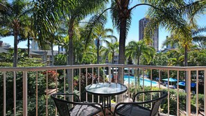 A balcony with a glass table and two chairs, overlooking a pool and palm trees. - Mari Court Resort (Surfers Paradise)