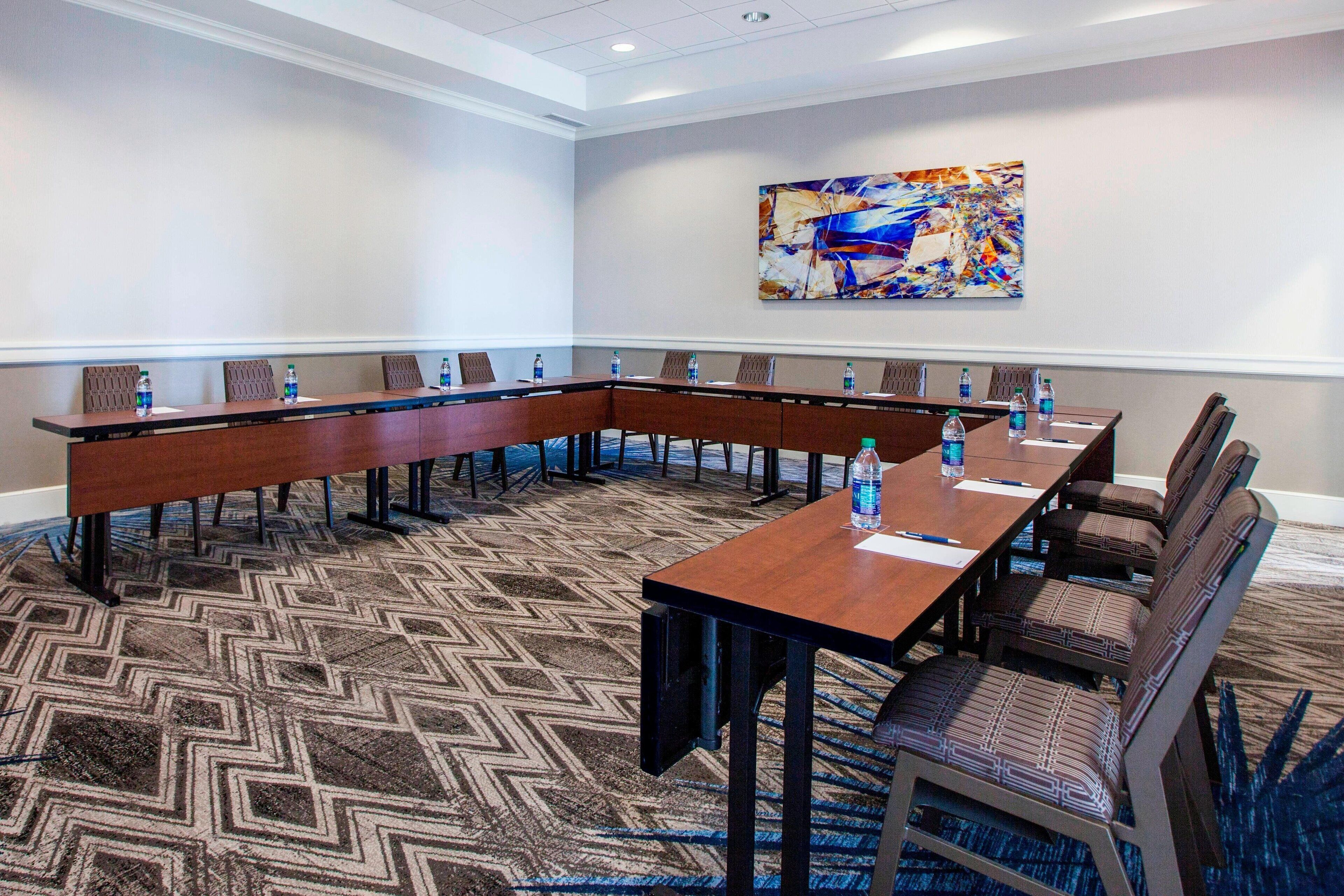A conference room with a long table and chairs, a patterned carpet, and a painting on the wall.