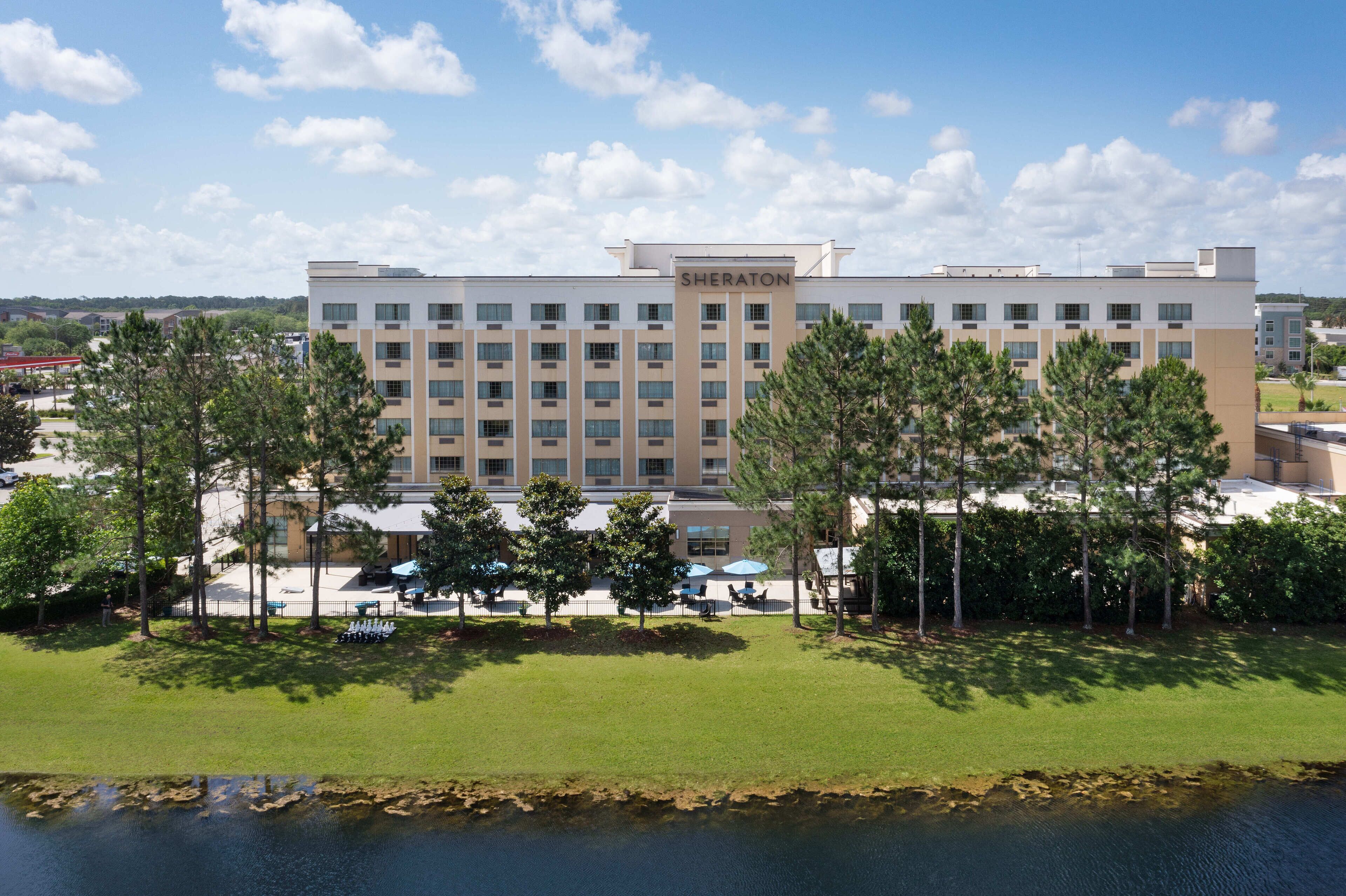 A Sheraton hotel with a modern design, featuring a central tower, multiple floors, and a well-maintained lawn with trees.