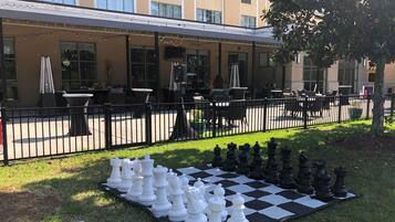 A large outdoor chess set on a checkered mat in front of a building with outdoor seating.