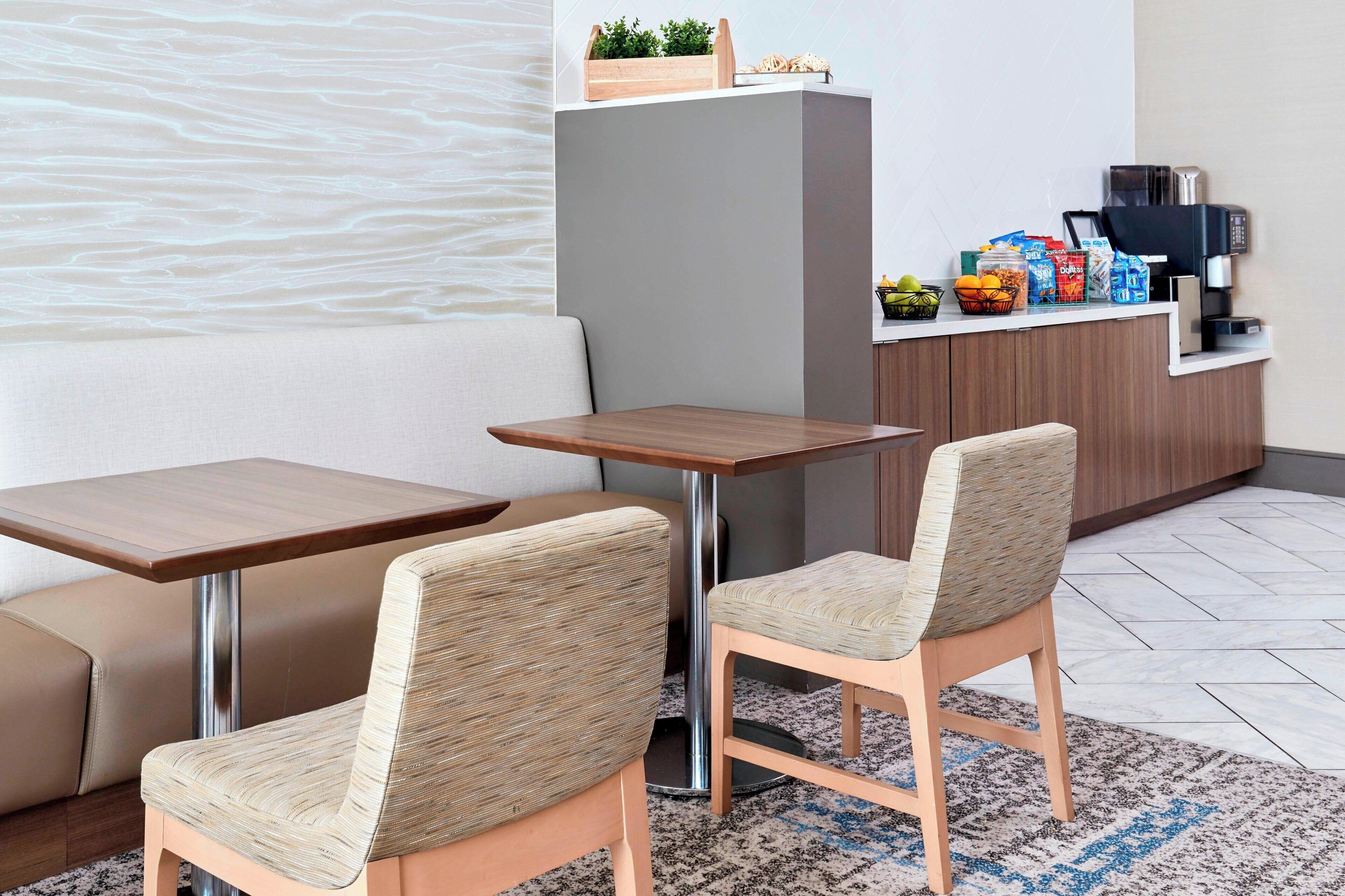 Una habitación de hotel moderna con sofá, dos mesitas de madera y una zona de kitchenette.