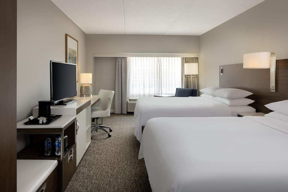 Habitación de hotel con dos camas, un escritorio con televisor, una silla y una ventana con cortinas.