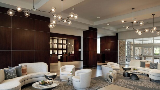 A modern lobby with a curved sofa, armchairs, and a coffee table. There are pendant lights and a large window with a view.
