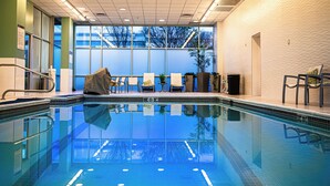 An indoor swimming pool with clear blue water, a tiled floor, and a view of trees through large windows.
