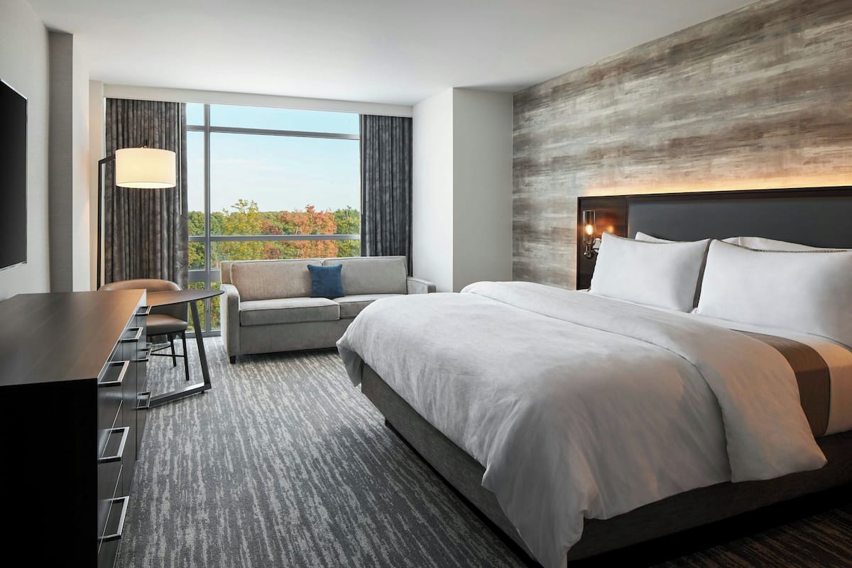 Ein modernes Hotelzimmer mit einem großen Bett, einer Couch, einem Schreibtisch und Blick ins Freie.