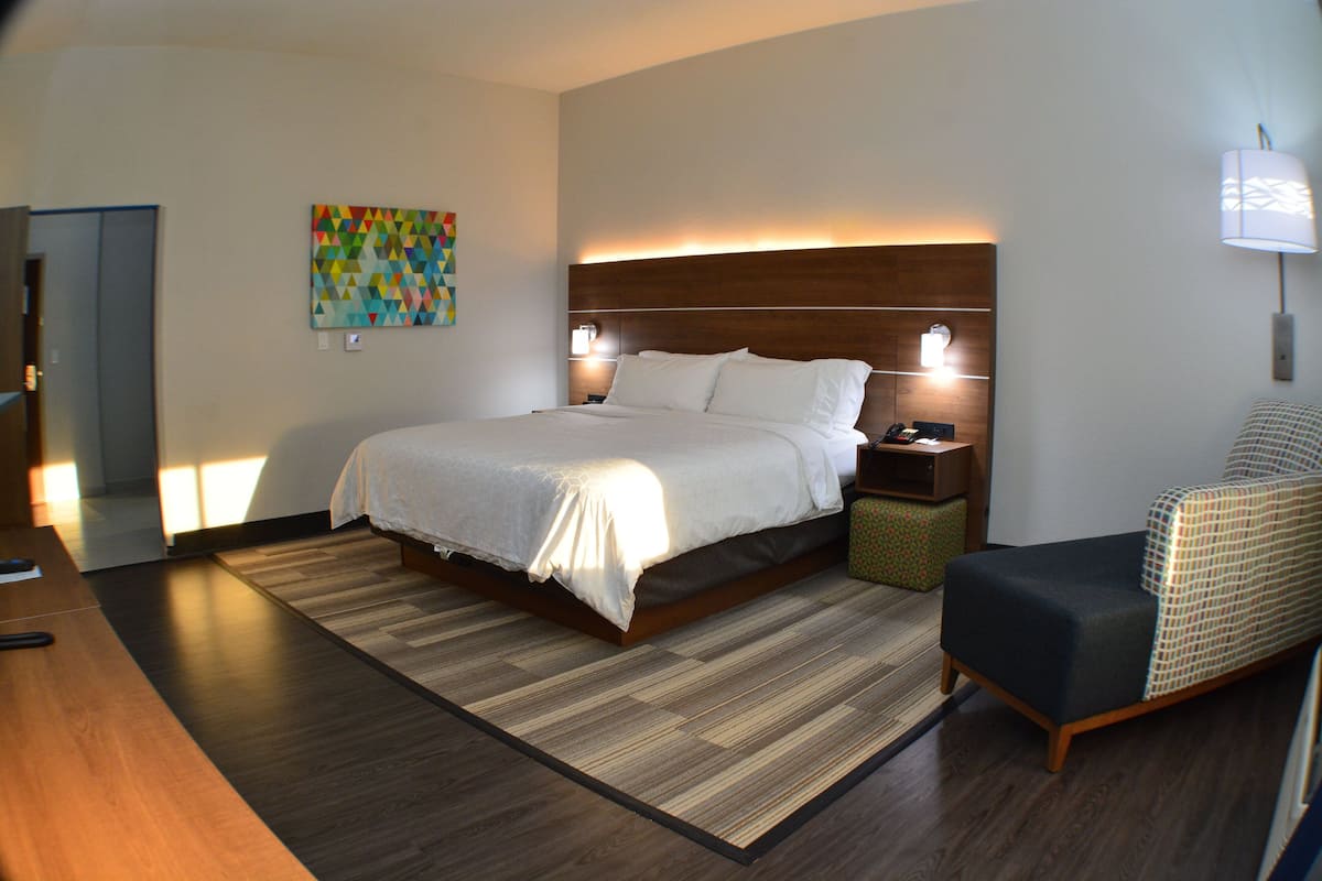 Une chambre d’hôtel avec un grand lit, des tables de chevet, une chaise, une œuvre d’art colorée accrochée au mur et un plancher en bois.