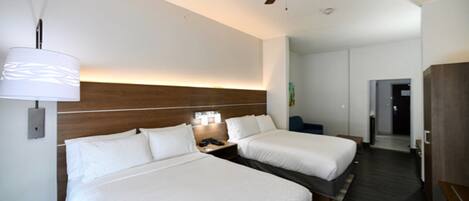 Quarto de hotel com duas camas, um ventilador de teto, mesa de cabeceira com luminária e cabeceira de madeira.