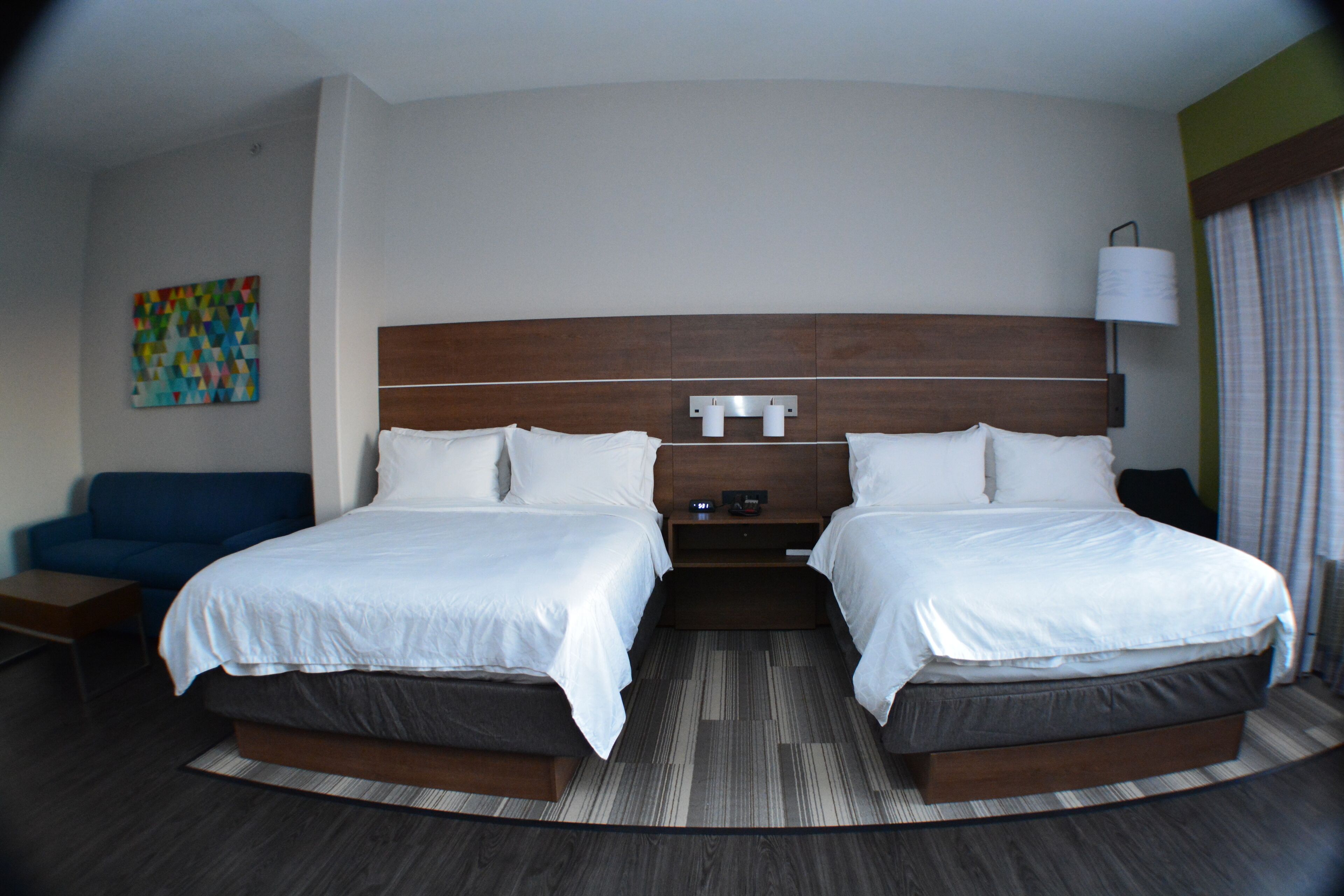 Una habitació d'hotel amb dos llits, una taula de nit, una làmpada i un quadre a la paret.