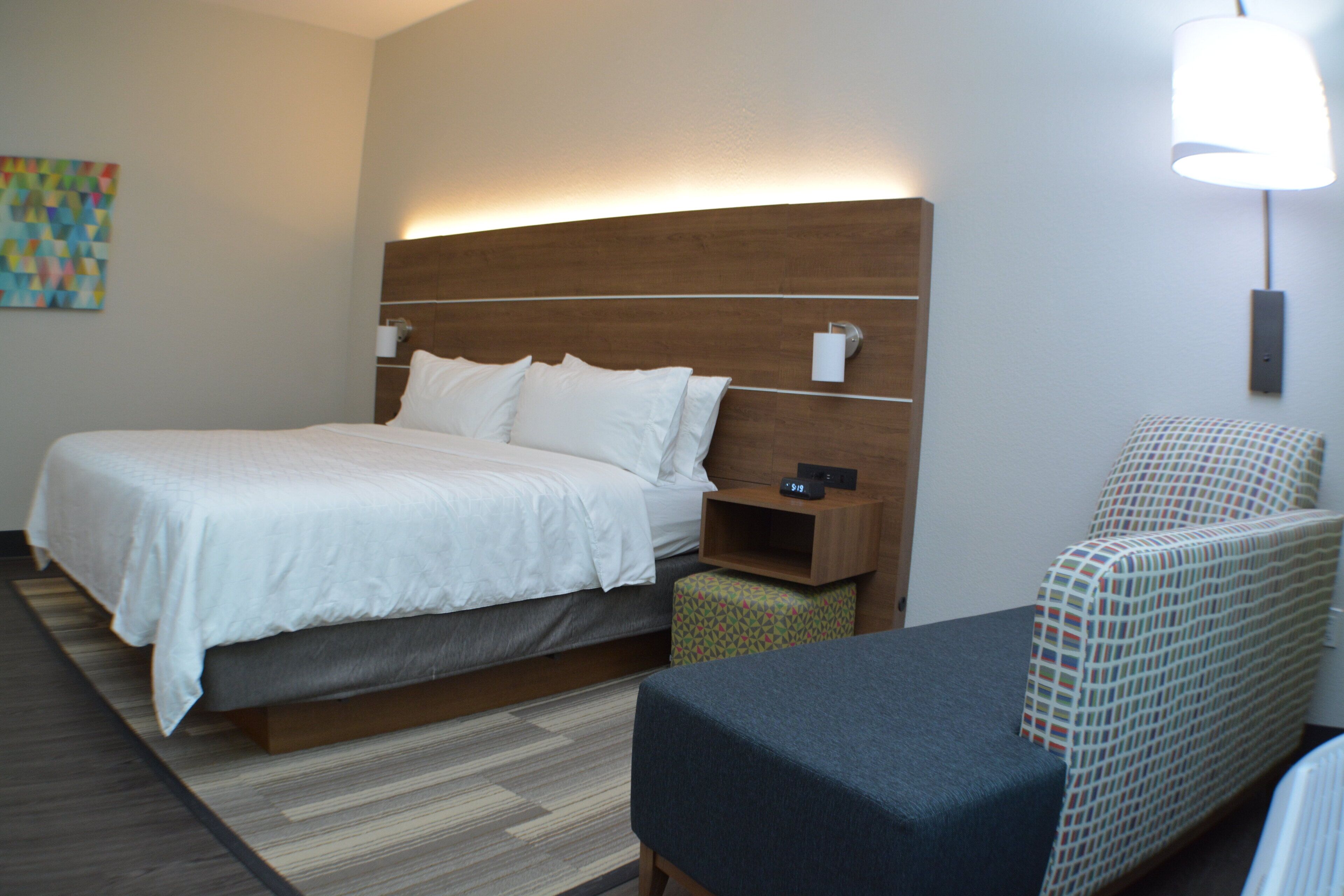 A hotel room with a large bed, bedside table, and a chair.