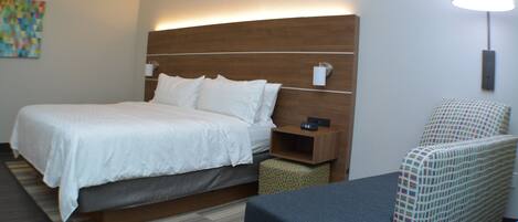 A hotel room with a large bed, bedside table, and a chair.