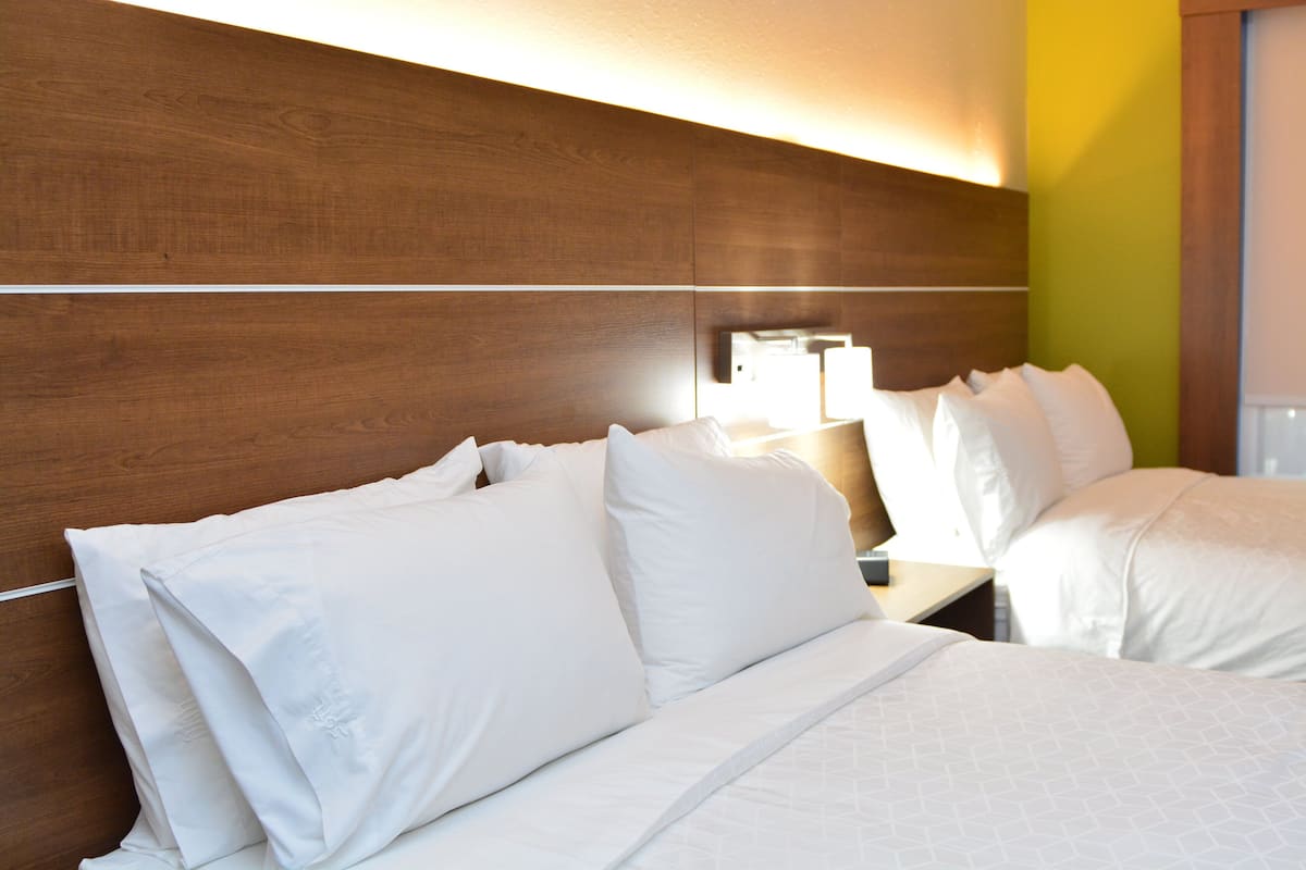 Une chambre d’hôtel avec une tête de lit en bois, du linge de lit blanc et une lampe de chevet.