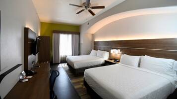 A hotel room with two beds, a desk, a television, and a ceiling fan.