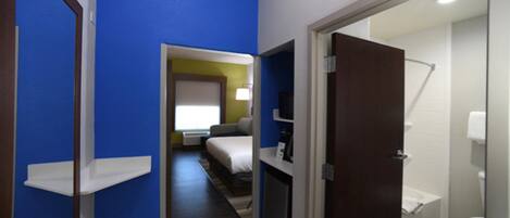 Habitación de hotel con una pared azul decorativa, una cama, mesita de noche, televisor y baño con inodoro y ducha.