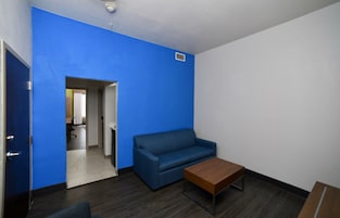 A room with a blue wall, a blue sofa, a wooden coffee table, and a door leading to another room.