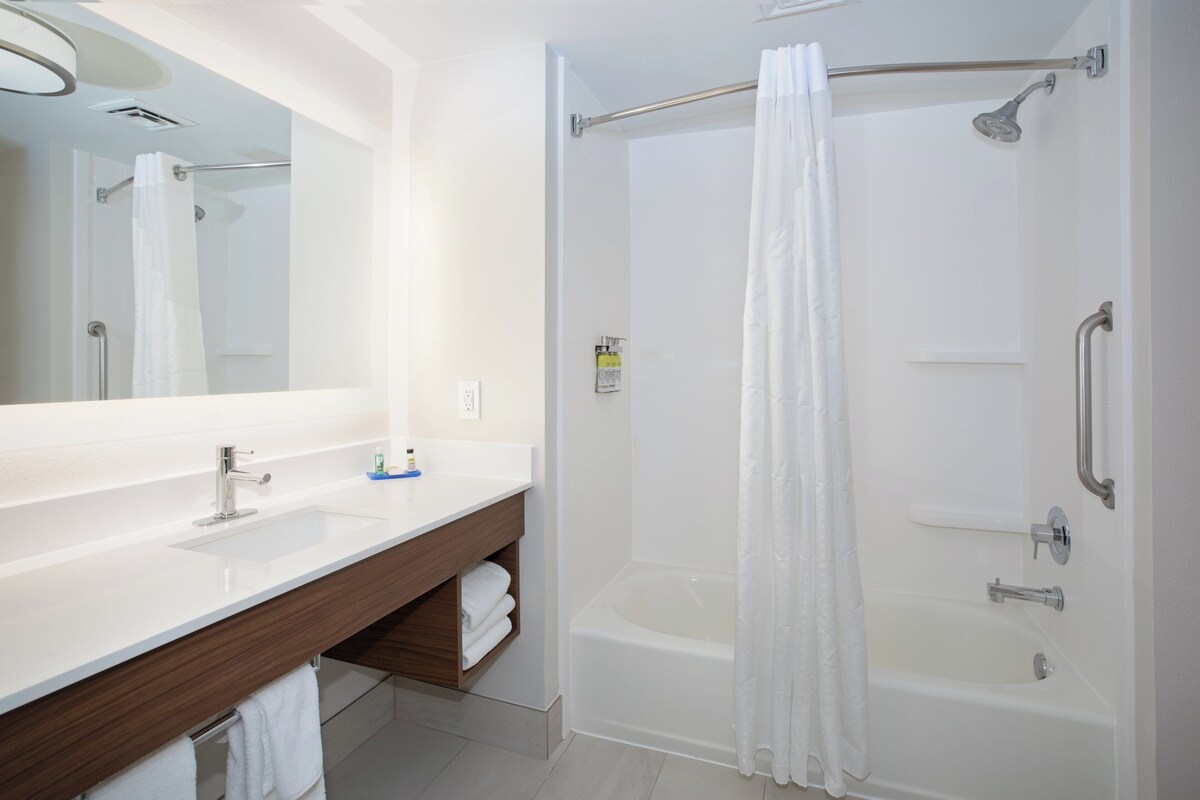 A modern bathroom with a large mirror, white sink, and a walk-in shower with a glass door.