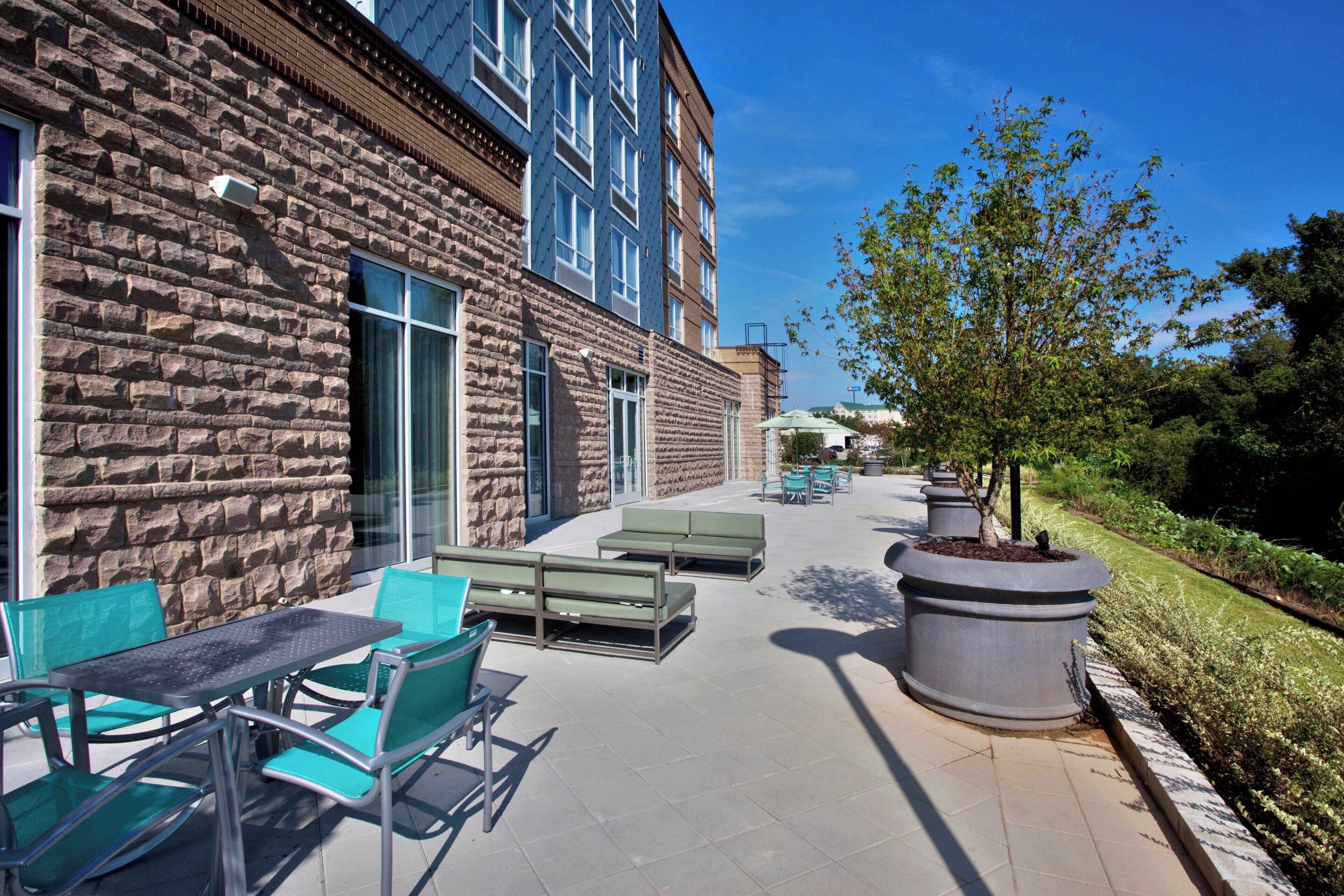 A courtyard with outdoor seating, a stone building, and a tree.