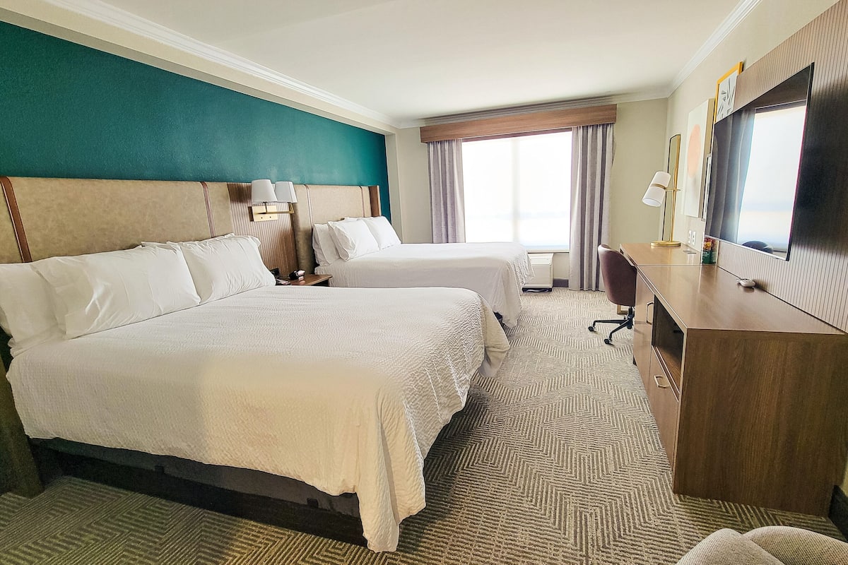 A hotel room with two beds, a desk, a chair, a TV, and a window with curtains.