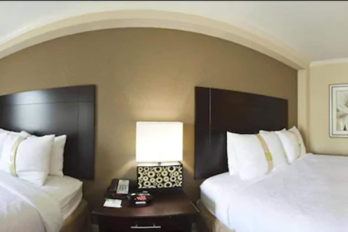 A hotel room with two beds, a nightstand, a lamp, and a framed picture on the wall.