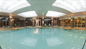 An indoor swimming pool with clear water, surrounded by lounge chairs and a glass wall.