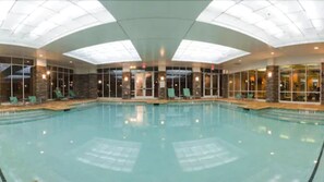 Une piscine intérieure à l’eau claire, entourée de chaises longues et dotée d’un mur en verre.
