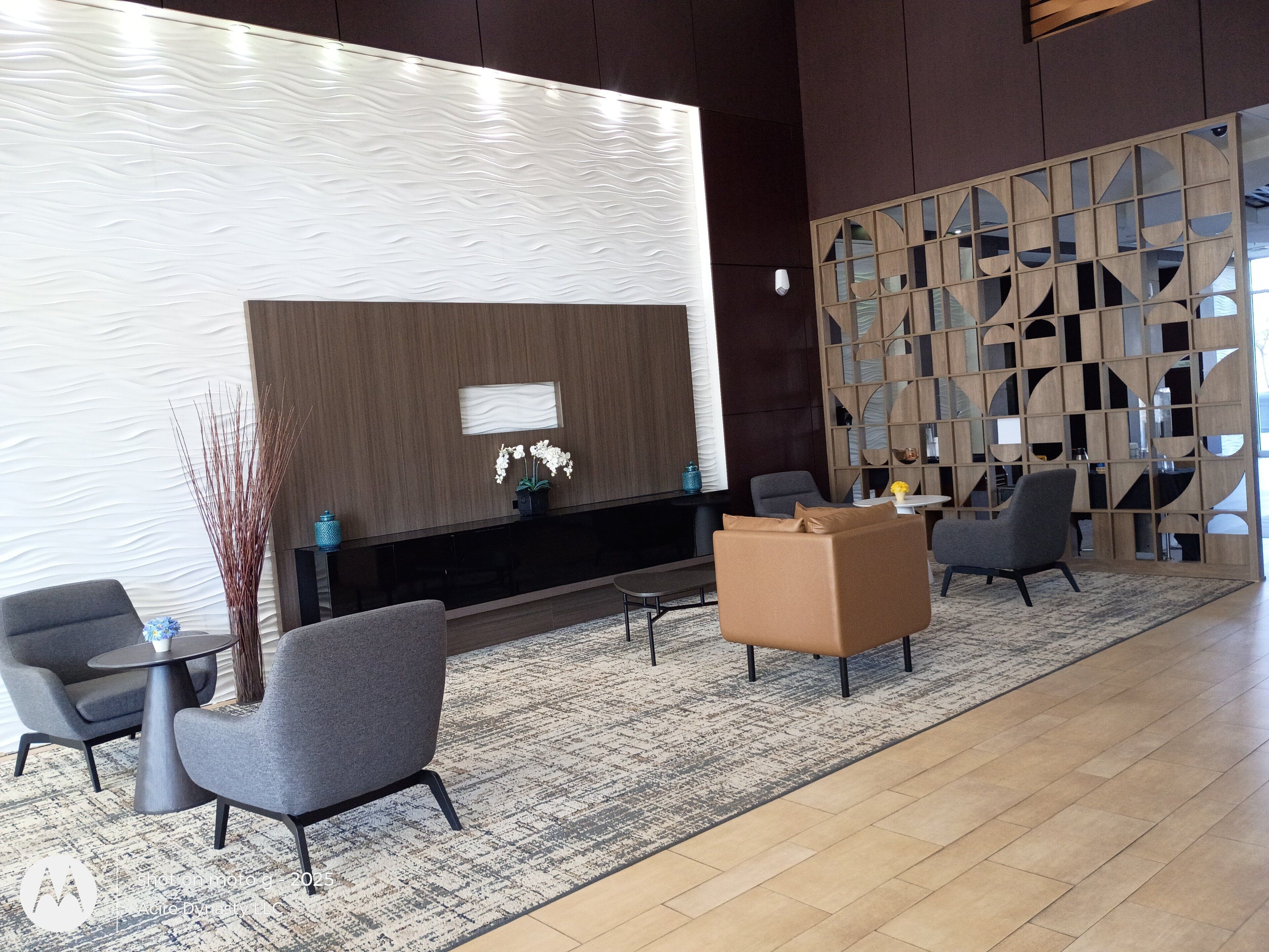 A modern lobby with a large wall-mounted display, seating area with sofas and chairs, and a decorative wooden partition.