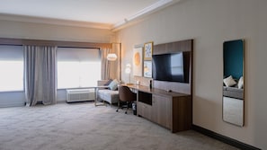 A hotel room with a bed, a desk, a chair, a TV, and a large window with curtains.