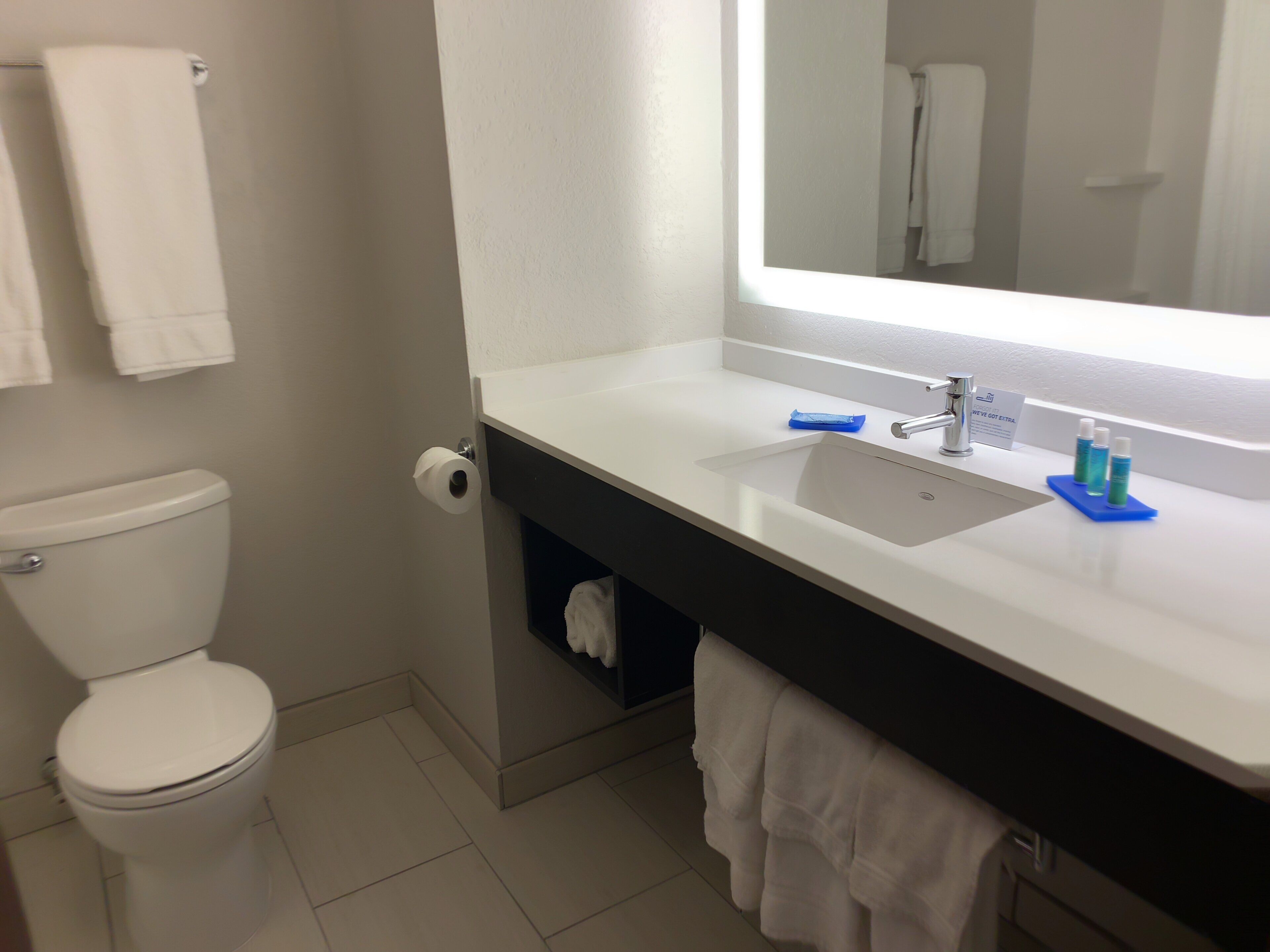 Een badkamer met toilet, wastafel, spiegel en handdoekhouder.
