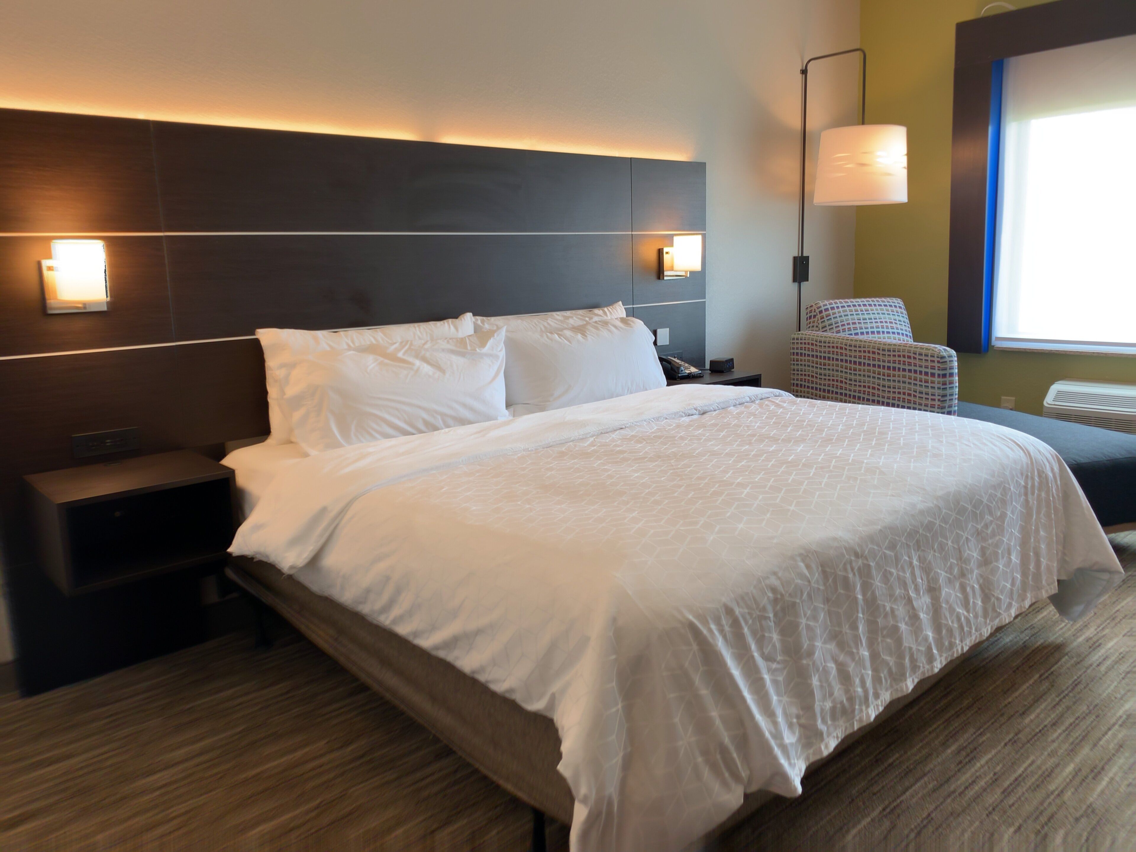 Een hotelkamer met een groot bed, nachtkastjes, een stoel en een wandlamp.