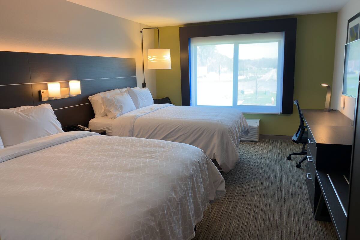 A hotel room with two beds, a desk, and a large window.