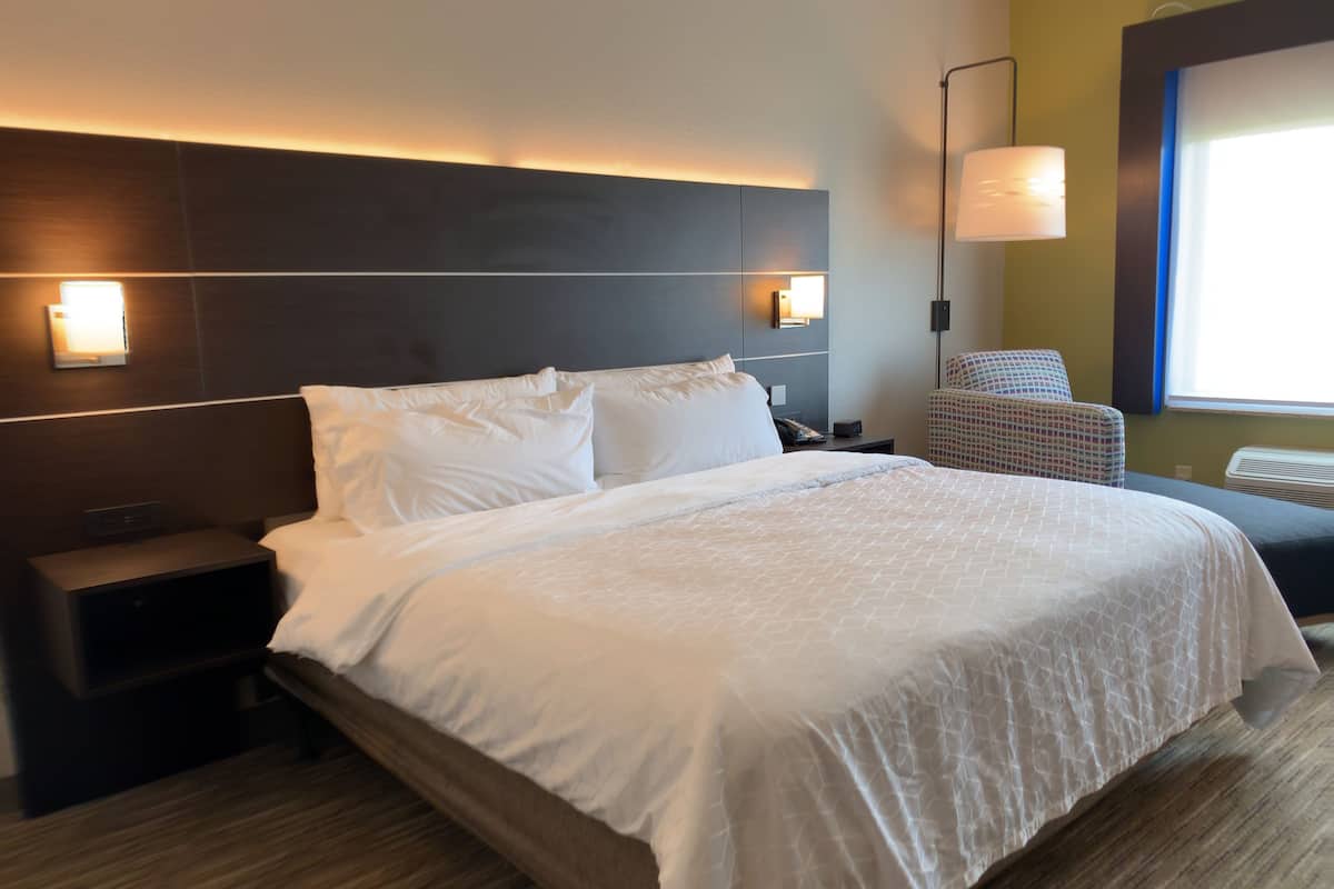 A hotel room with a large bed, bedside tables, a chair, and a lamp.