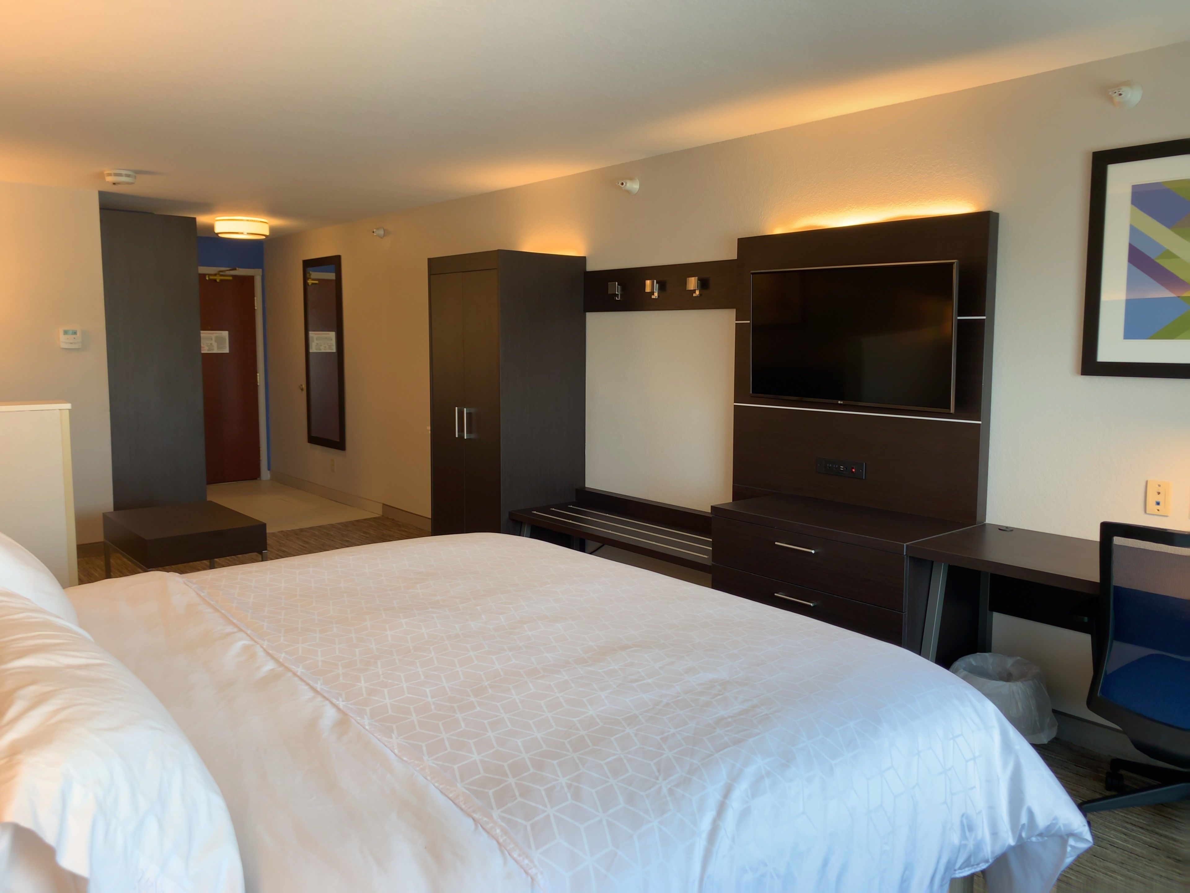 A hotel room with a large bed, a TV, a wardrobe, and a desk.