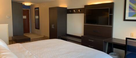 A hotel room with a large bed, a TV, a wardrobe, and a desk.