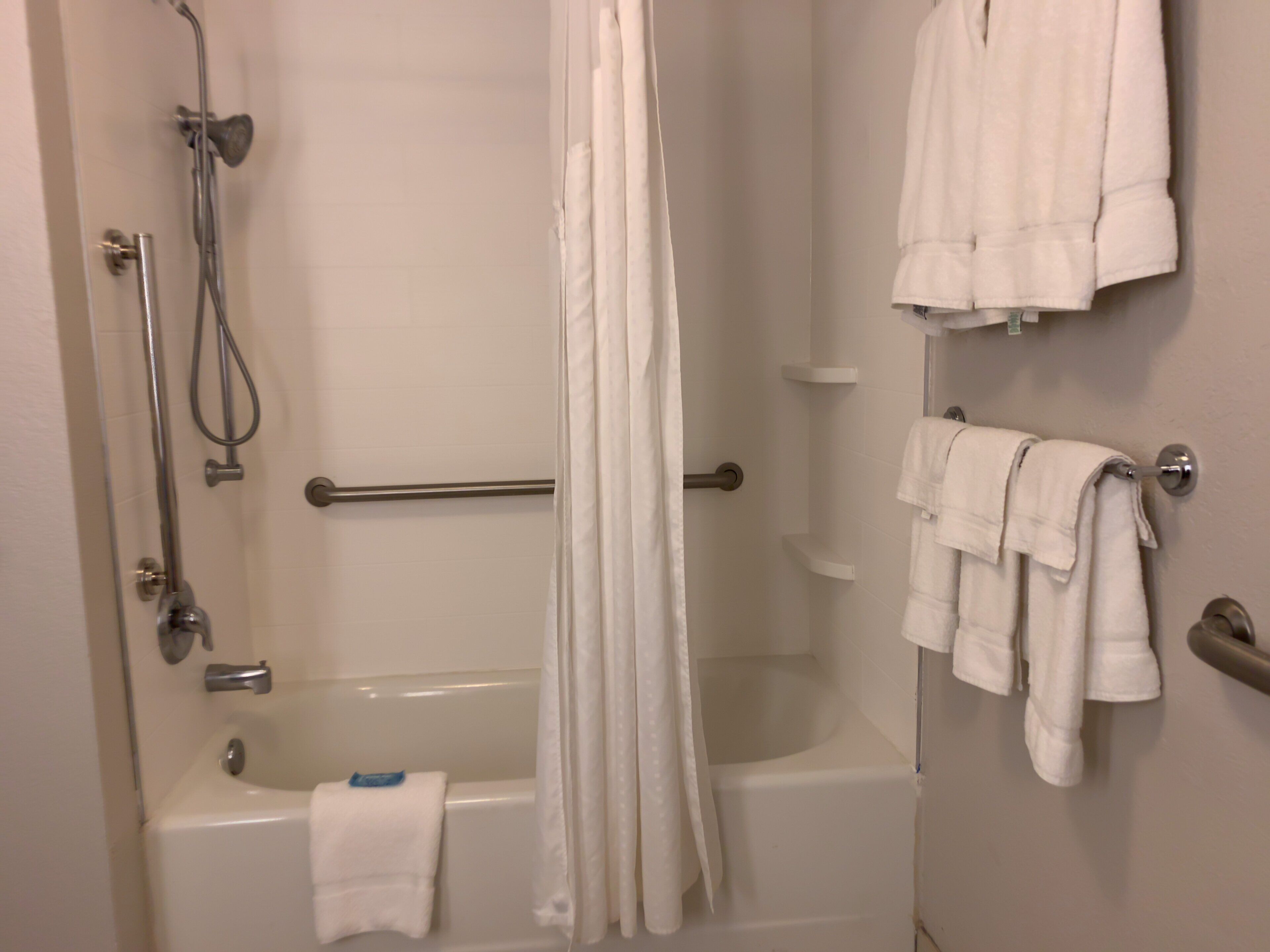 A bathroom with a bathtub, shower, and a towel rack with multiple towels.
