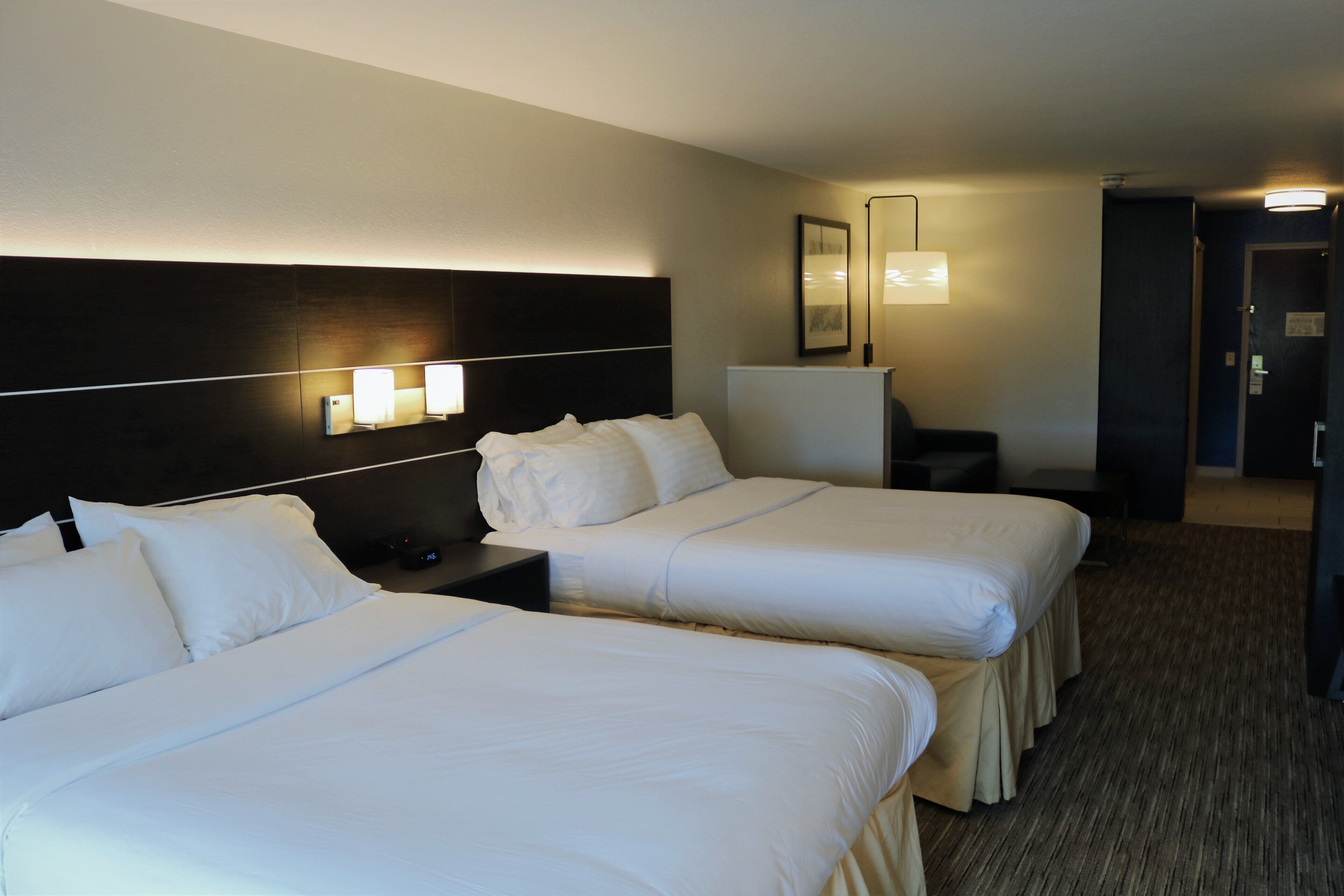 Quarto de hotel com duas camas, uma mesa de cabeceira, escrivaninha e uma luminária.