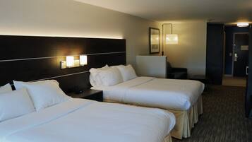 Quarto de hotel com duas camas, uma mesa de cabeceira, escrivaninha e uma luminária.
