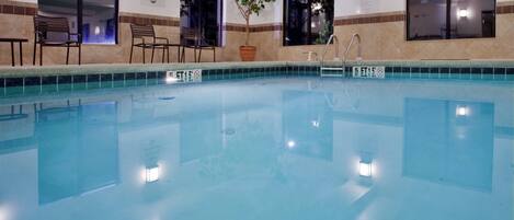 Una piscina interior cristalina donde no se permite bucear, rodeada de sillas y una planta en maceta.