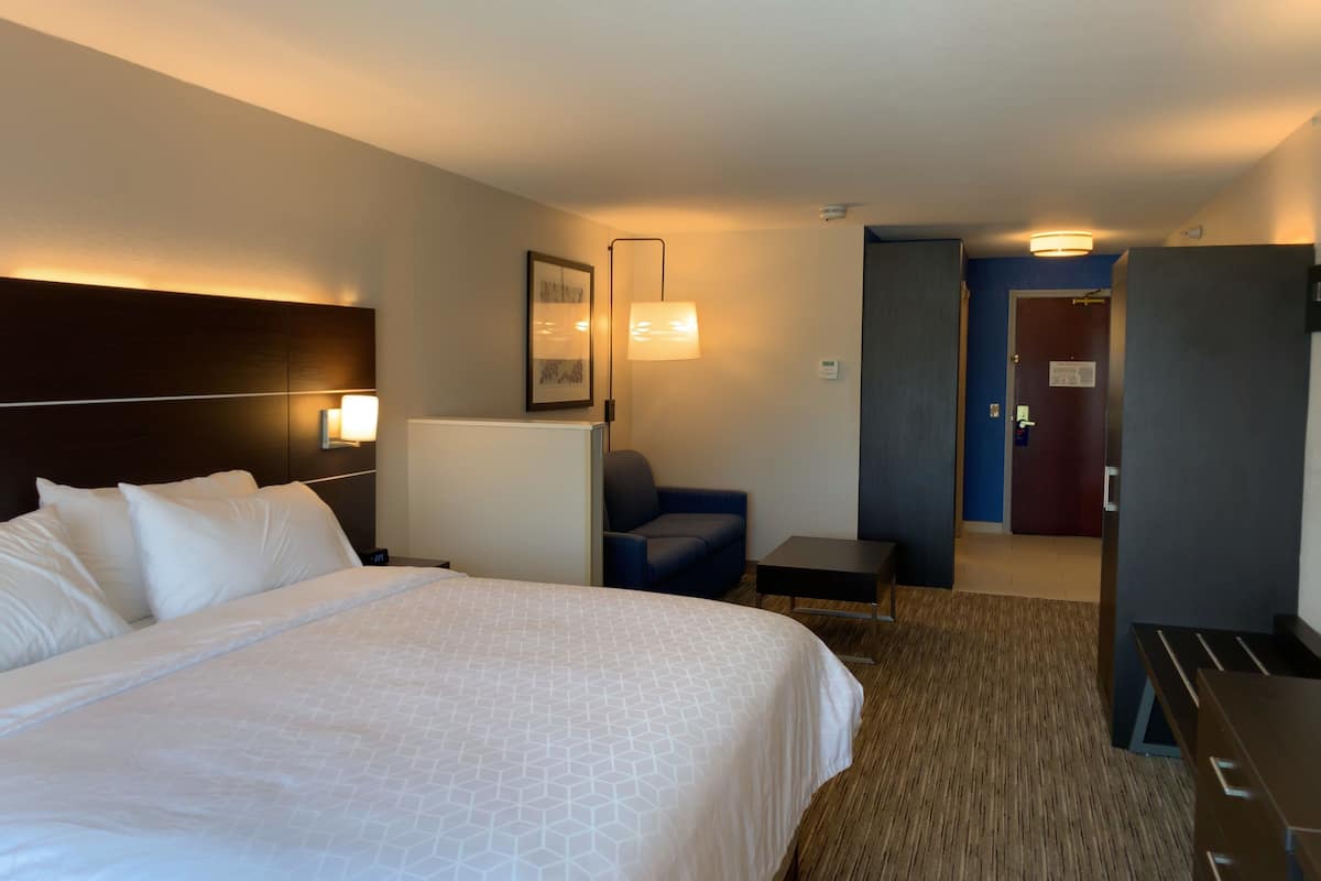 A hotel room with a large bed, a desk, a chair, and a door leading to another room.