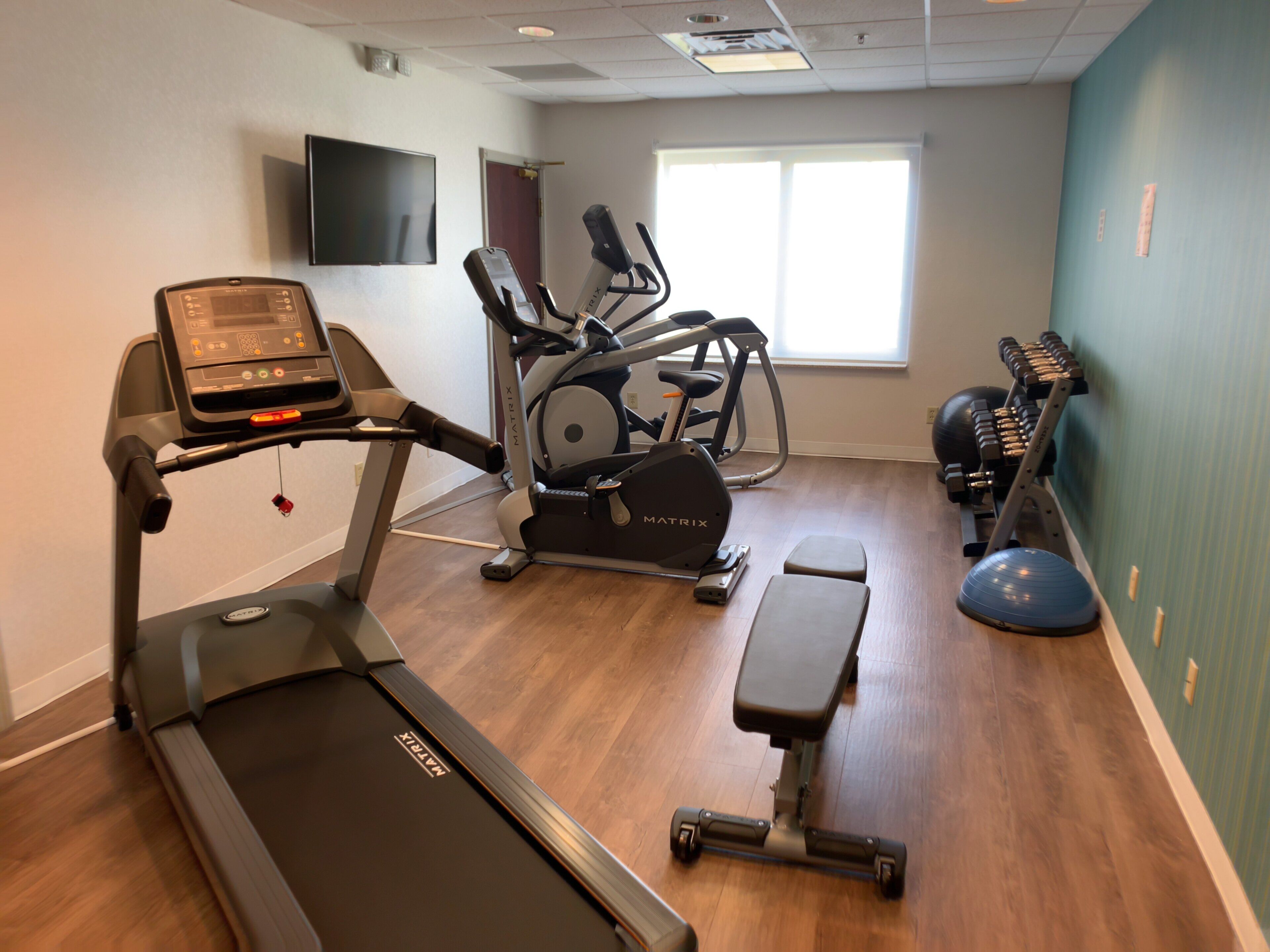 A gym with a treadmill, elliptical, stationary bike, and free weights.